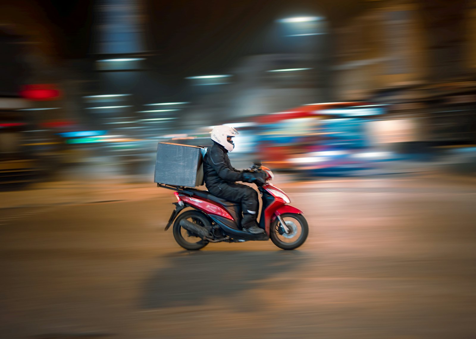 Repartidor en moto llevando un pedido de noche por la ciudad